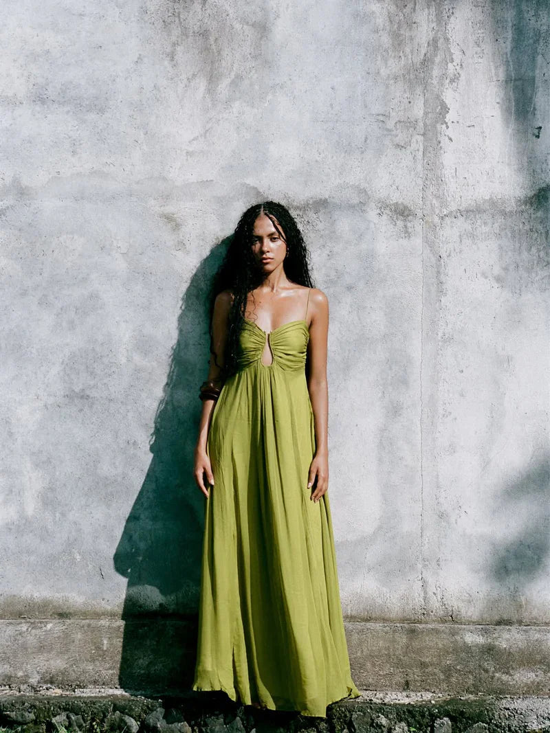 Front view of the women's olive green gathered bust keyhole maxi dress, showcasing the keyhole and bust details against a concrete wall.