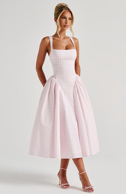 Full-length view of a woman in a light pink gingham square neck midi dress with a structured bodice and voluminous skirt, wearing pink heels.