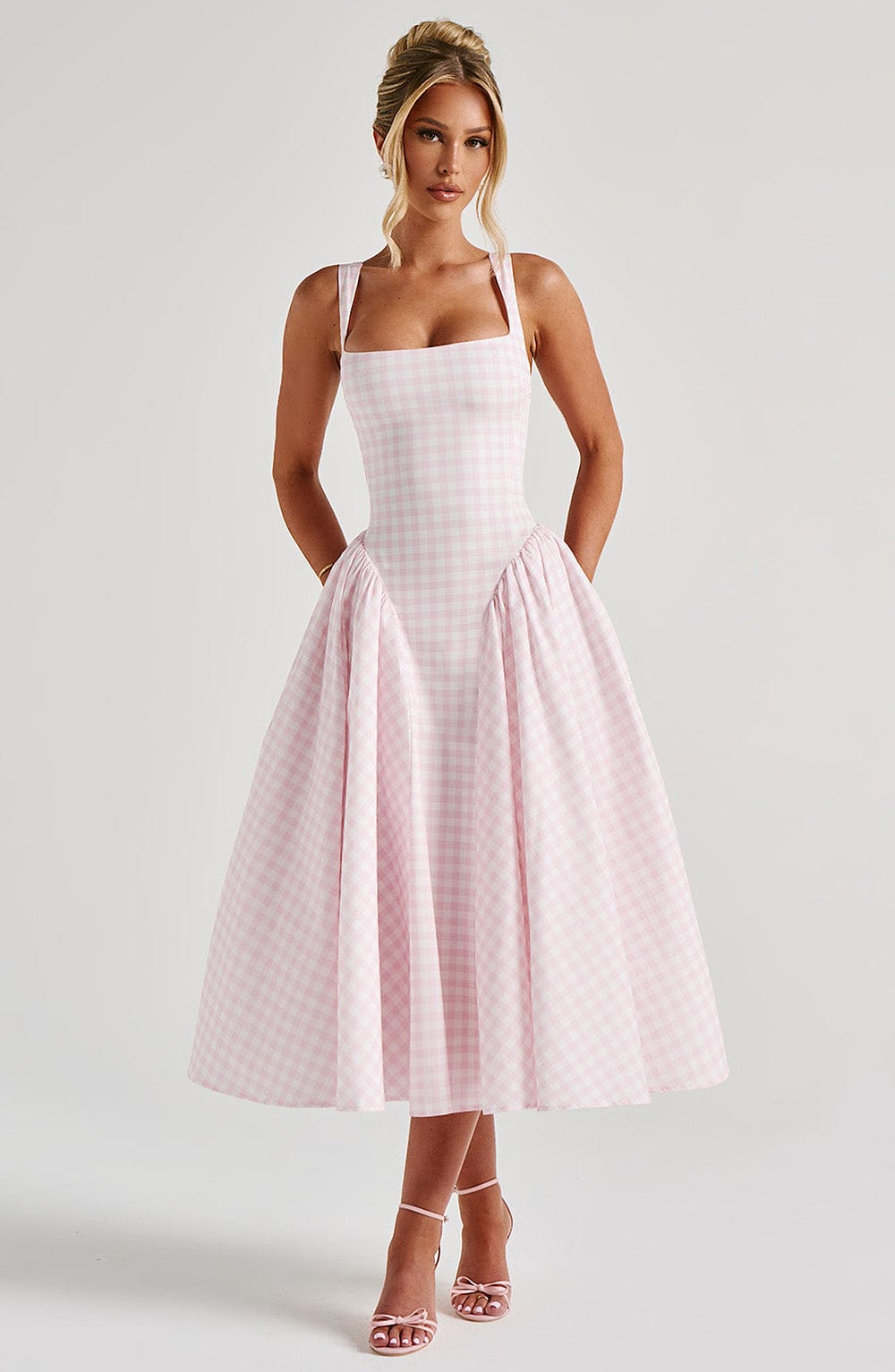 Woman posing in a pink gingham square neck midi dress, featuring a fitted bodice and a full, gathered skirt, with pink strappy heels.