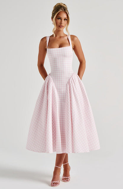 Woman posing in a pink gingham square neck midi dress, featuring a fitted bodice and a full, gathered skirt, with pink strappy heels.
