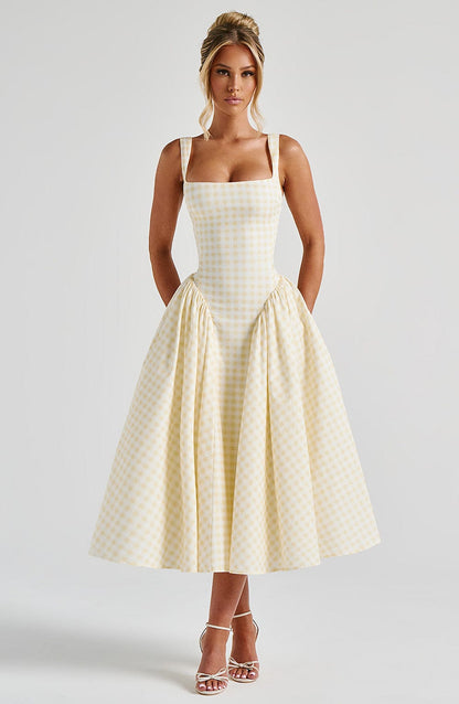 Woman wearing a light yellow gingham square neck midi dress with a fitted bodice and a full, pleated skirt, paired with white heels.