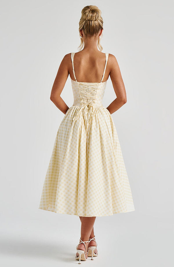 Back view of a light yellow gingham square neck midi dress, featuring a lace-up corset detail on the back and a full skirt.