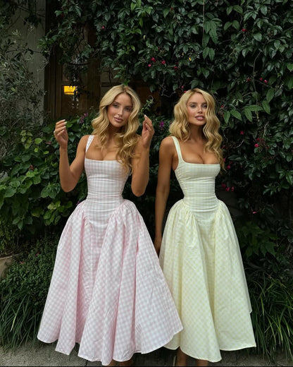 Two women wearing square neck midi dresses, one in pink gingham and one in yellow gingham, with full skirts, standing outdoors.