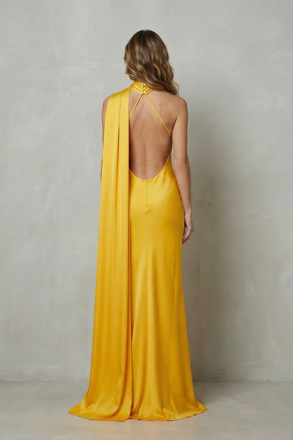 Back view of the yellow formal halter draped open back maxi dress, highlighting the open back design and long flowing train.