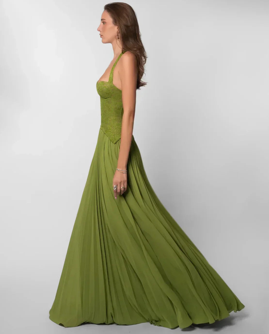 Side profile of the olive green formal halter neck maxi dress, emphasizing the flowing pleated skirt and corset top.