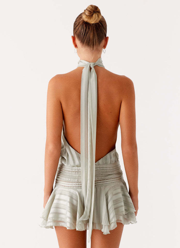 Back view of the light sage green halter neck mini dress, highlighting the open back and long tie detail.
