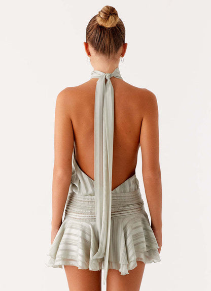 Back view of the light sage green halter neck mini dress, highlighting the open back and long tie detail.