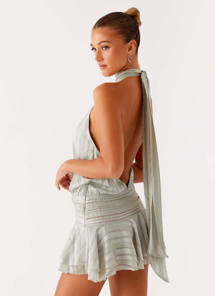 Three-quarter back view of the light sage green halter neck mini dress, emphasizing the open back and tie detail.