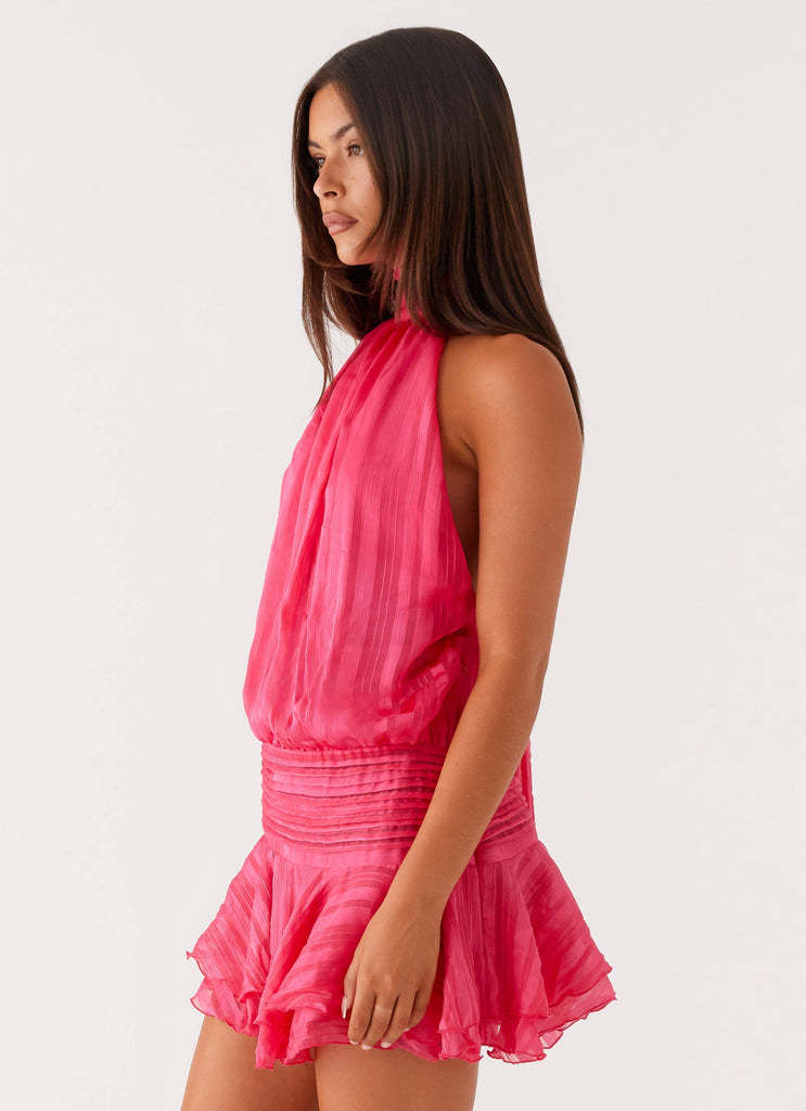 Side profile of the hot pink halter neck mini dress, highlighting the flowy material and the short, ruffled hem.