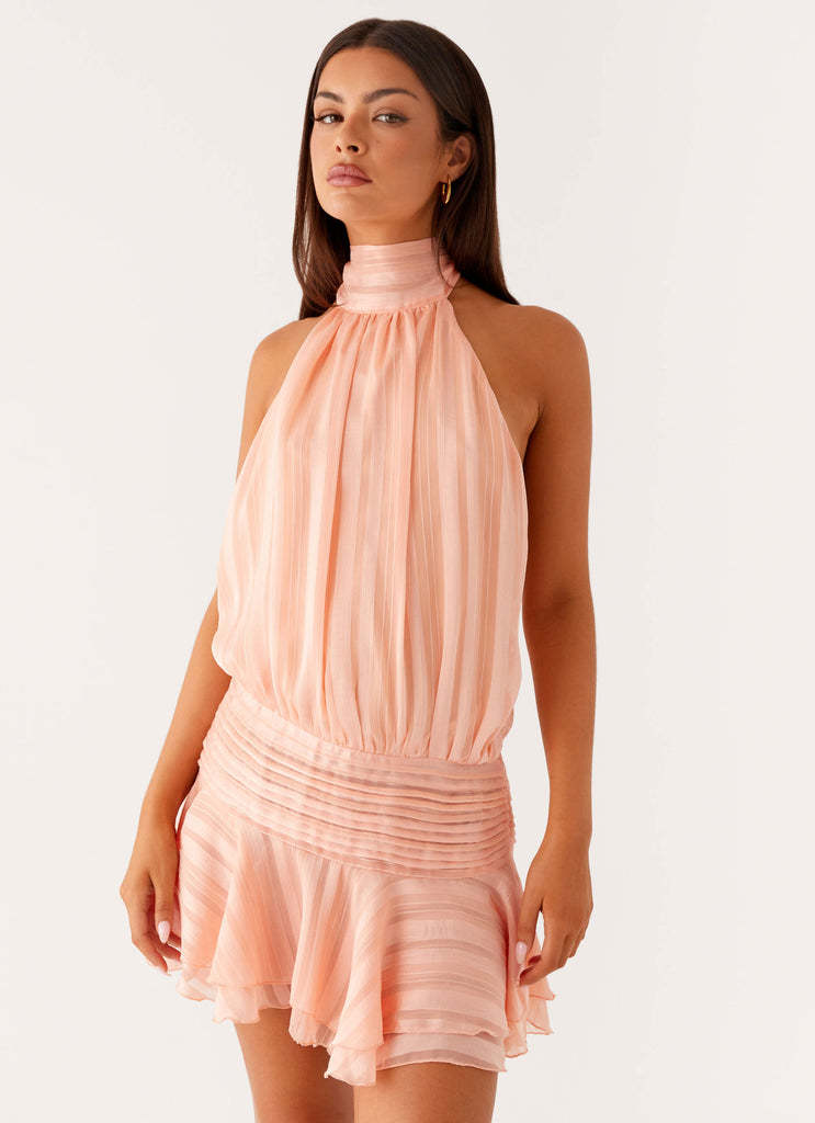 Close-up of a peach halter neck mini dress, featuring a ruched waistline and subtle striped texture, worn by a model.