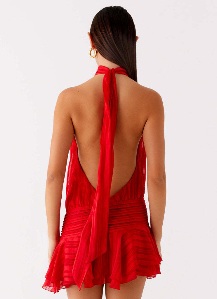 Back view of a red halter neck mini dress, highlighting the open back and long, flowing tie detail.