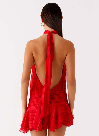 Back view of a red halter neck mini dress, highlighting the open back and long, flowing tie detail.