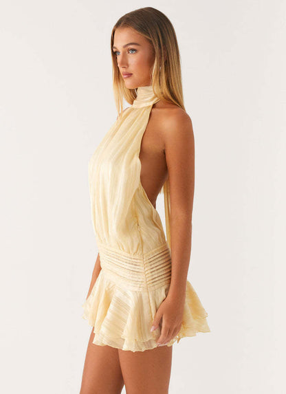 Left side view of a women's light yellow halter neck ruched waist mini dress with a flowing skirt.