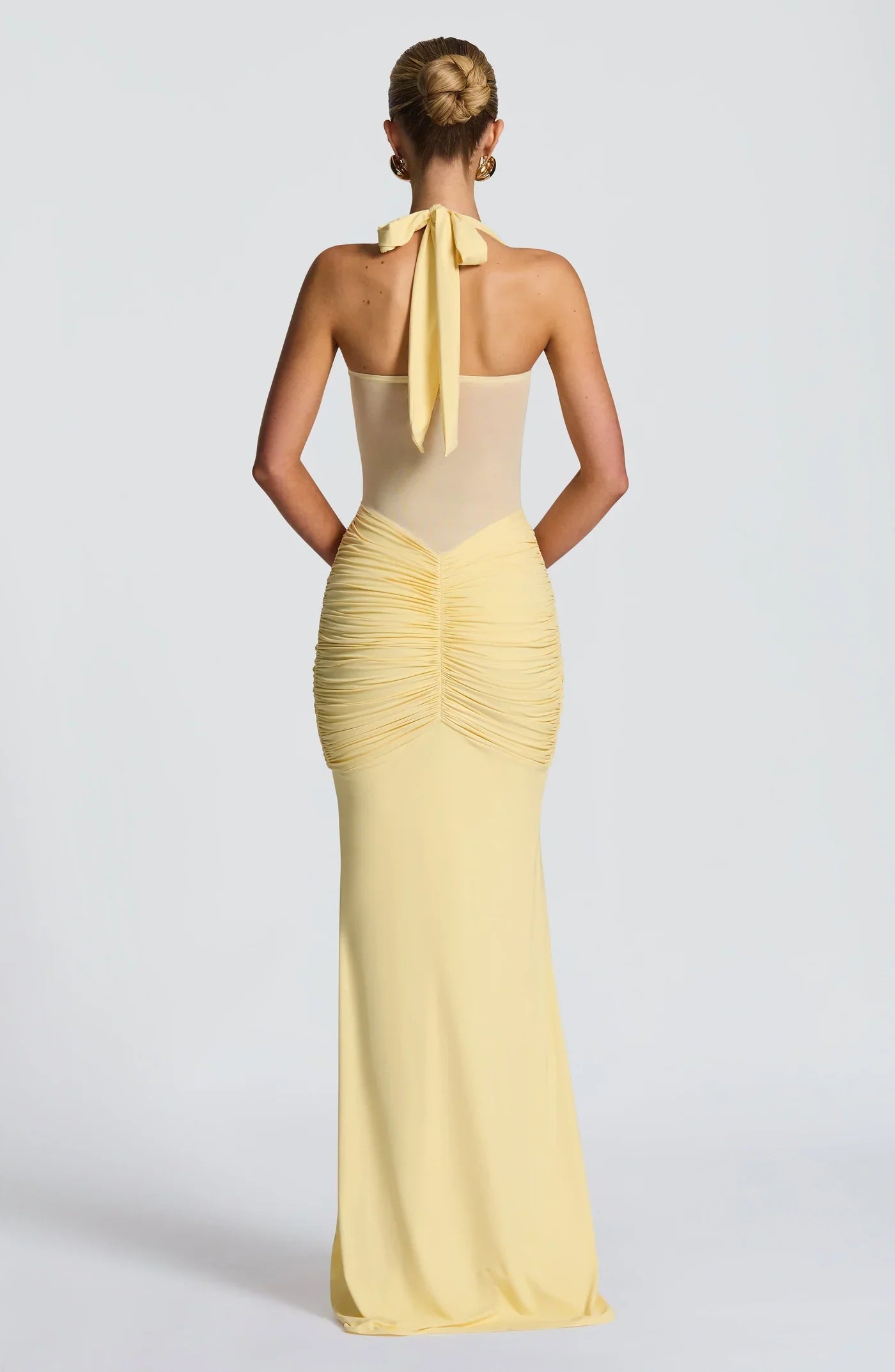 Back view of a yellow halter neck maxi dress with a tied bow at the neck and ruched detailing on the back.
