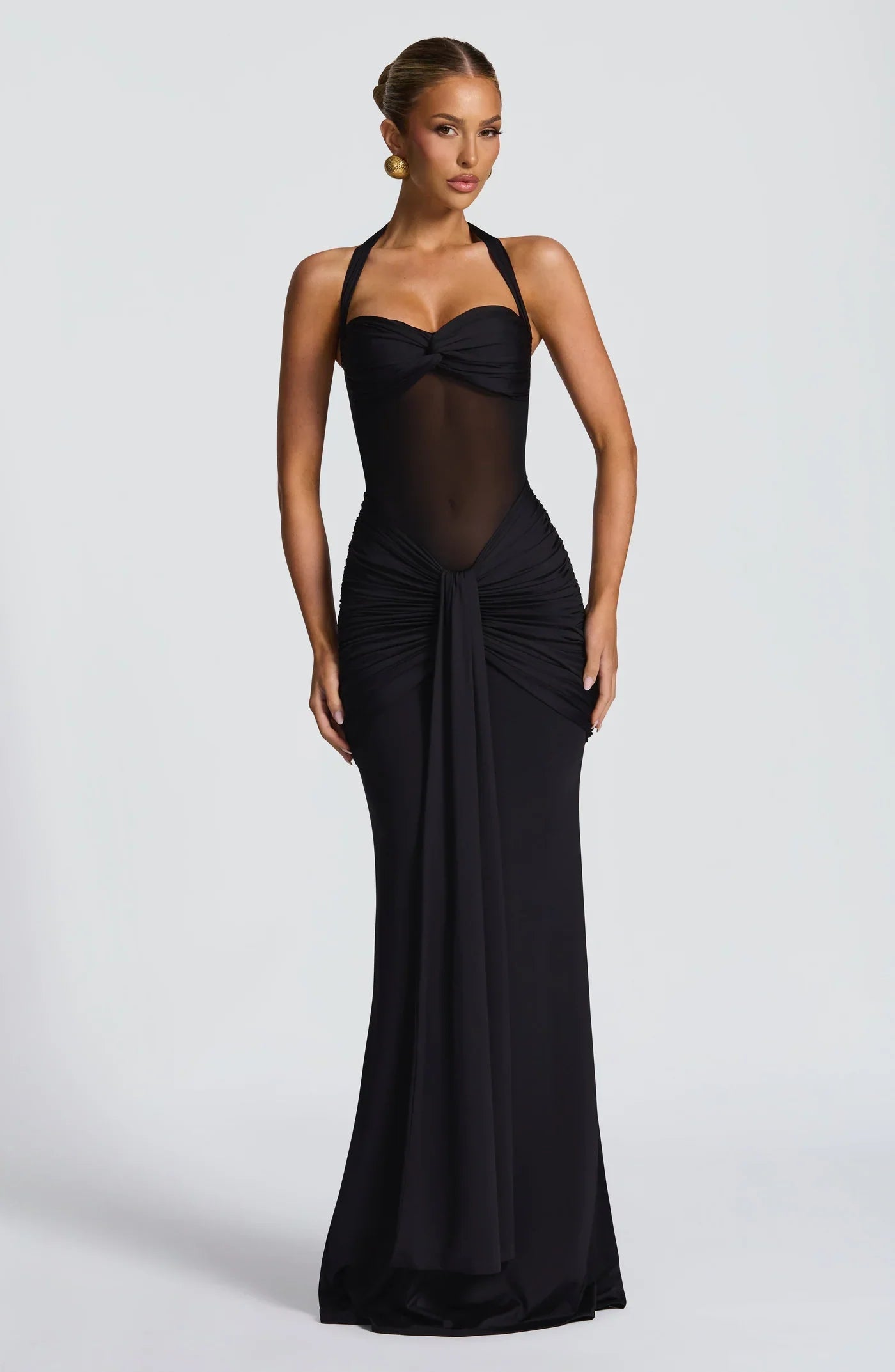 Full-length black halter neck twisted ruched maxi dress with sheer mesh paneling for an elegant evening look.