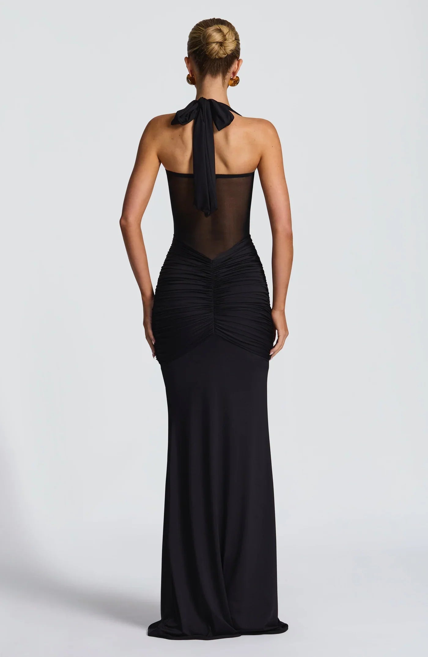 Back view of a black halter neck maxi dress with a tied bow and ruched detailing on the lower back.