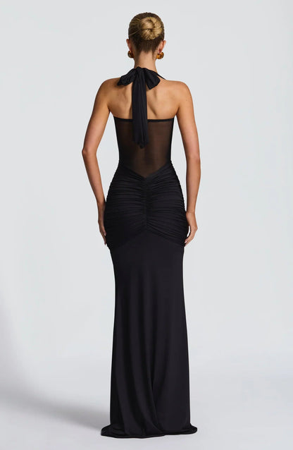 Back view of a black halter neck maxi dress with a tied bow and ruched detailing on the lower back.