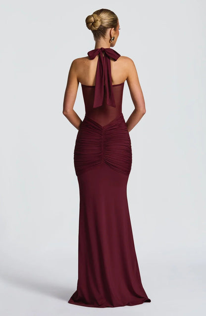 Back view of a burgundy halter neck maxi dress with a tied bow and elegant ruched detailing on the rear.