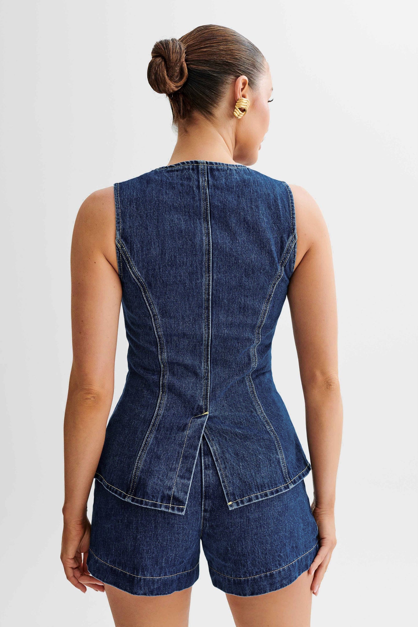 Back view of sleeveless dark wash denim vest and matching high waisted denim shorts set