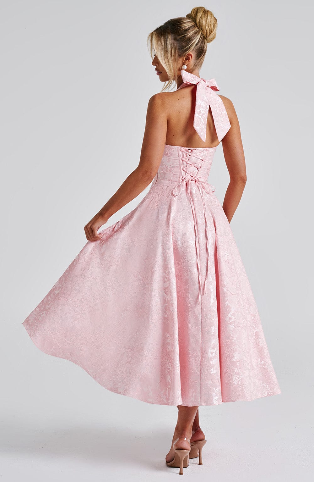 Back view of a pink jacquard halter neck midi dress, revealing the bow detail and corset lacing on the bodice.