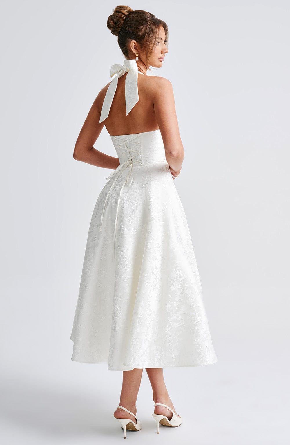 Back view of a white jacquard halter neck midi dress with a tied bow at the neck and corset lacing detail.