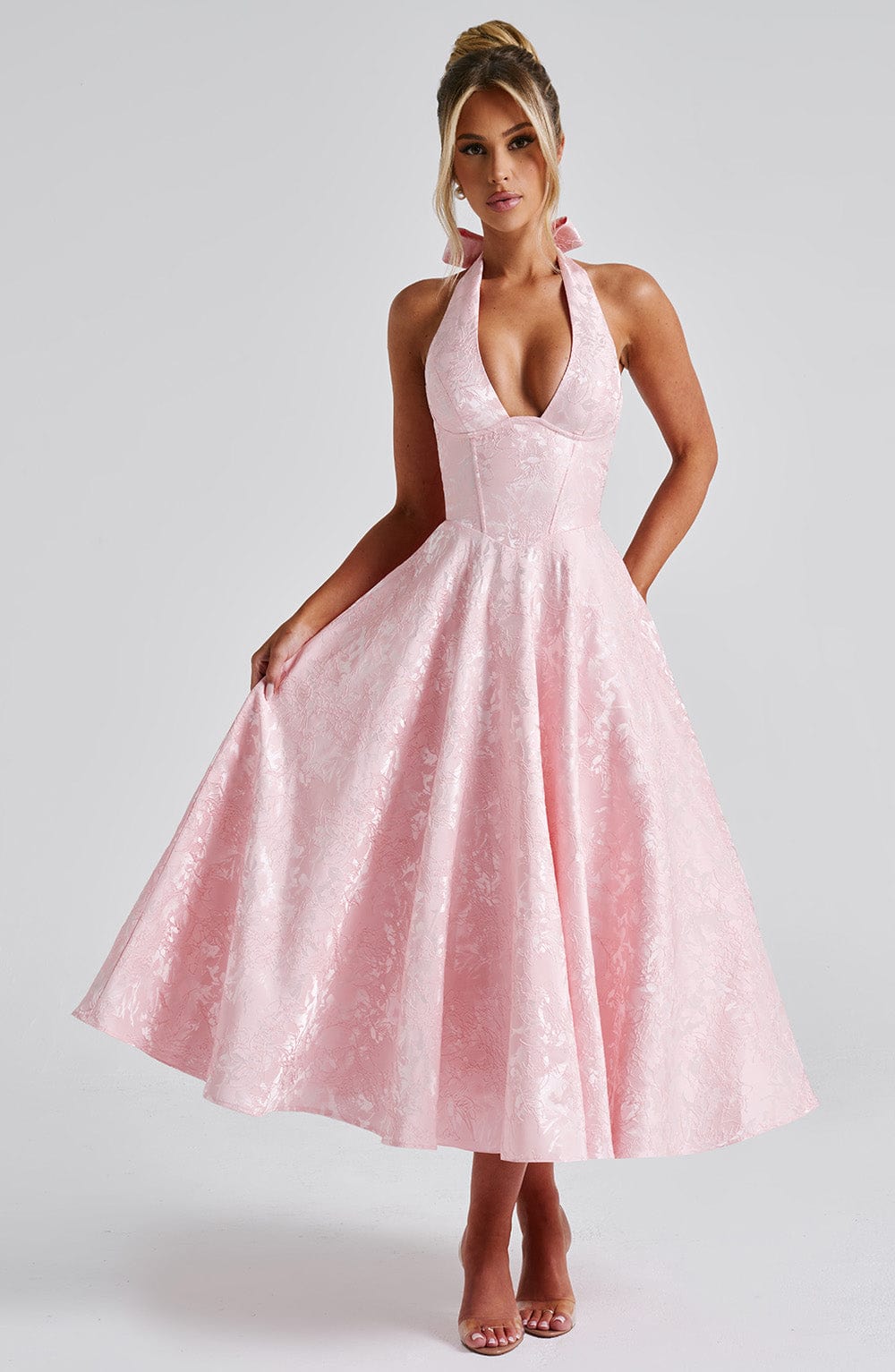 Light pink jacquard halter neck midi dress with a full skirt and deep V-neck, featuring a bow detail at the neck.