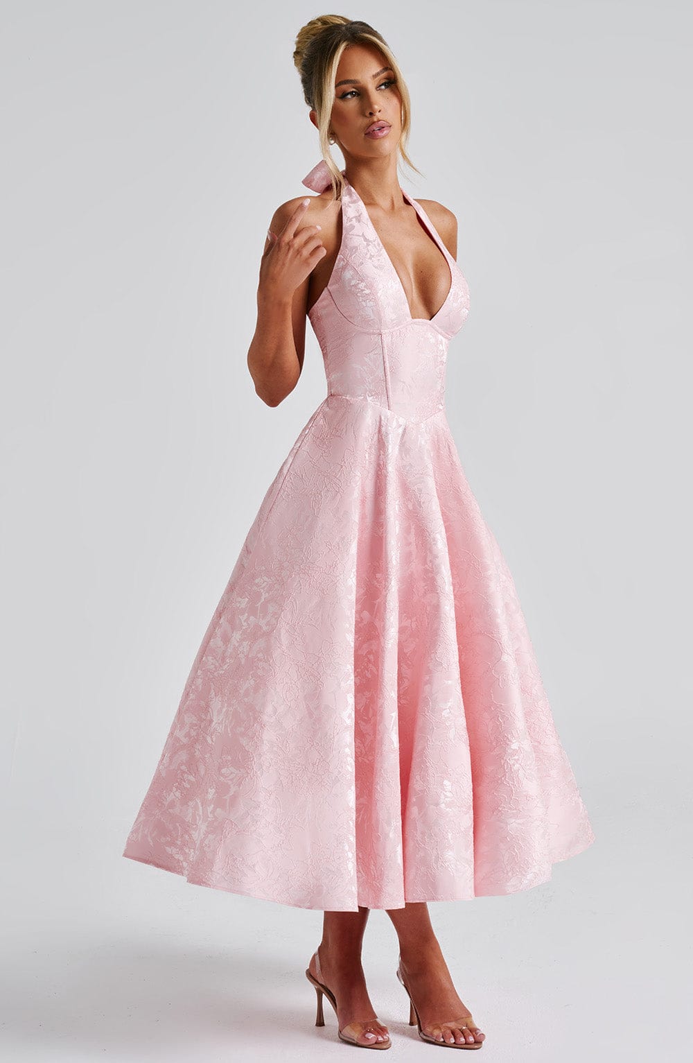 Side view of a pink jacquard halter neck midi dress, showing the full skirt and a bow detail at the back of the neck.