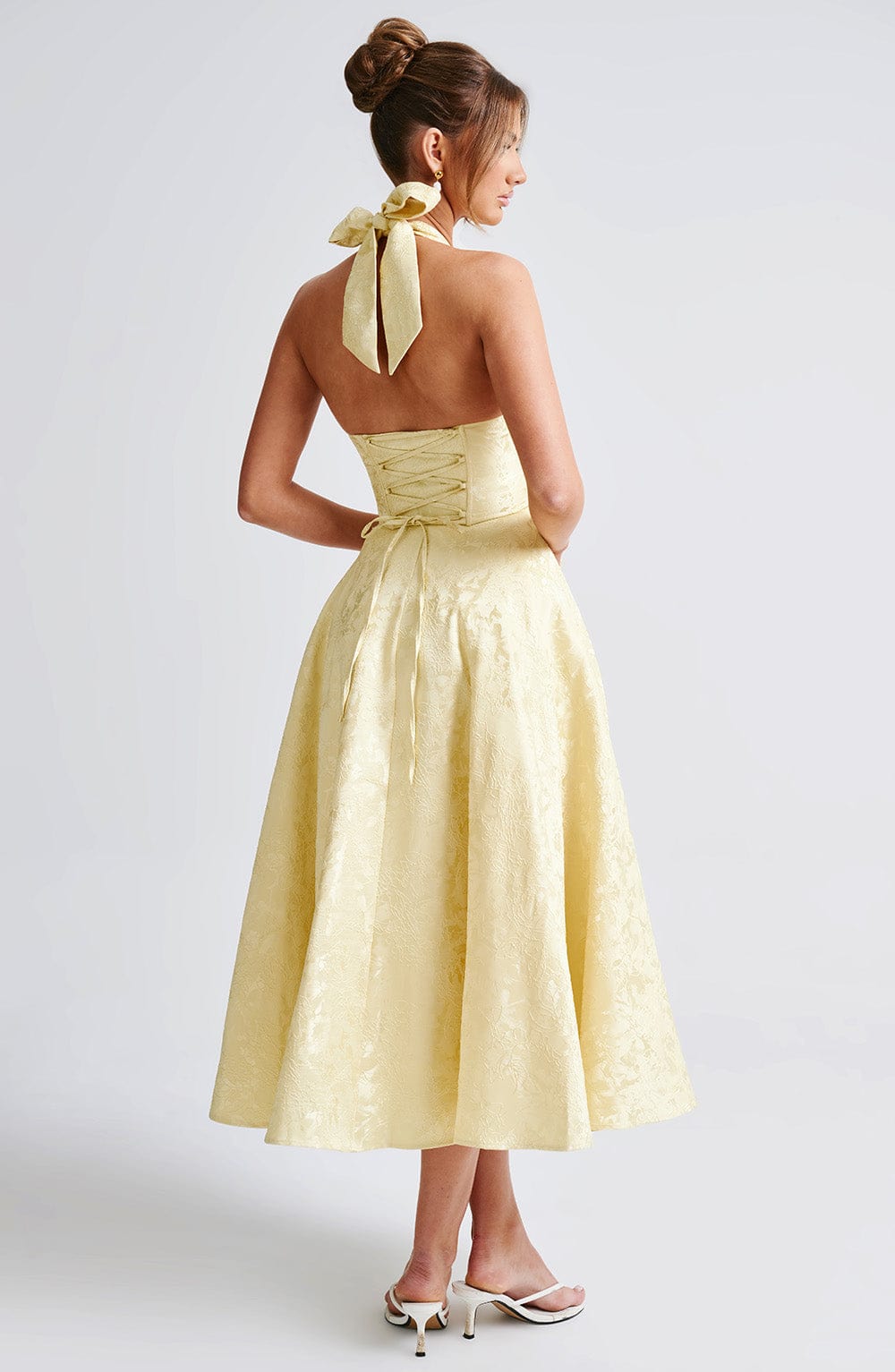 Back view of a yellow jacquard halter neck midi dress, showcasing the lace-up corset detail and bow tie neck.