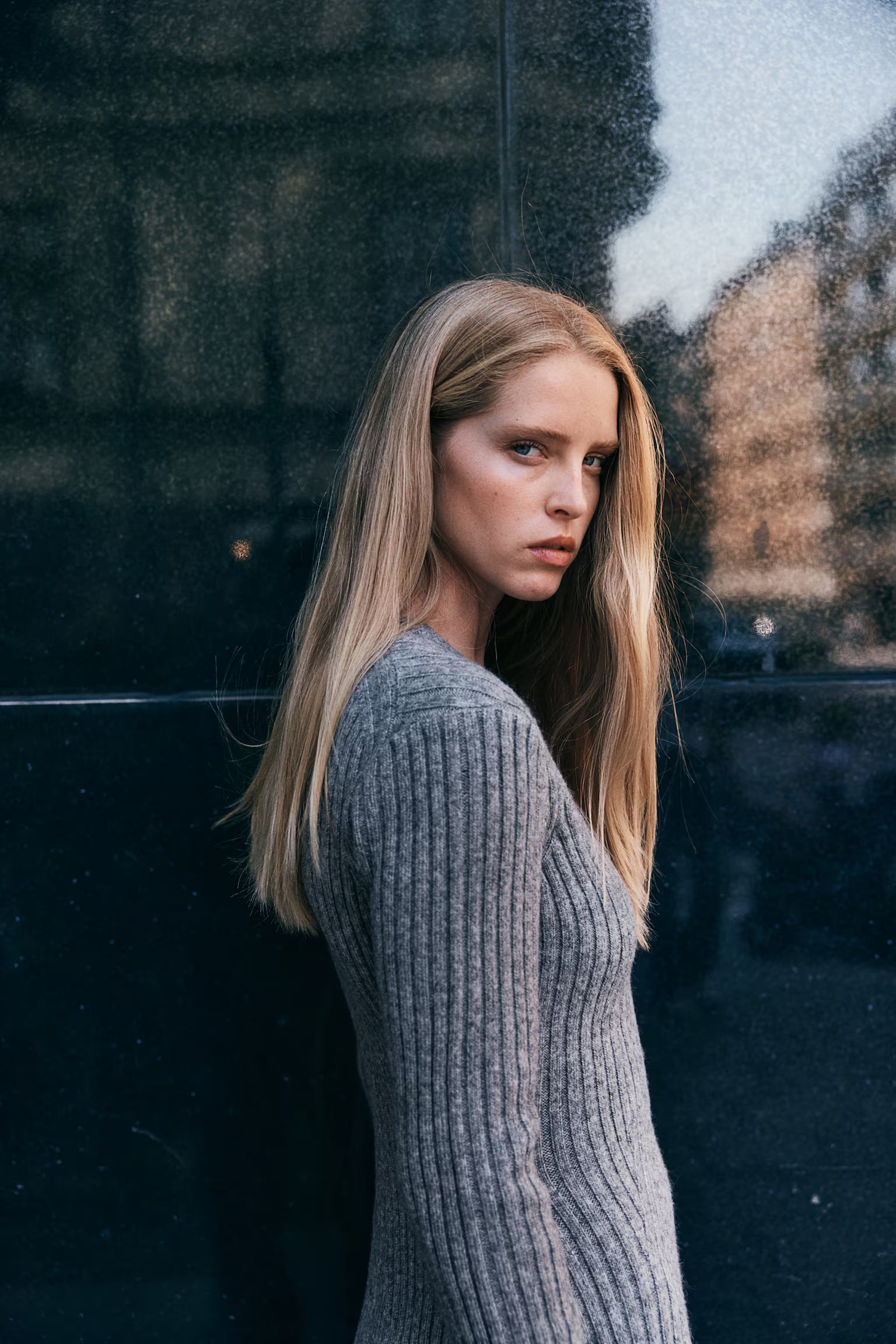 Side profile of a woman wearing a grey knit long sleeve ribbed mini dress, showing the texture of the ribbed fabric.