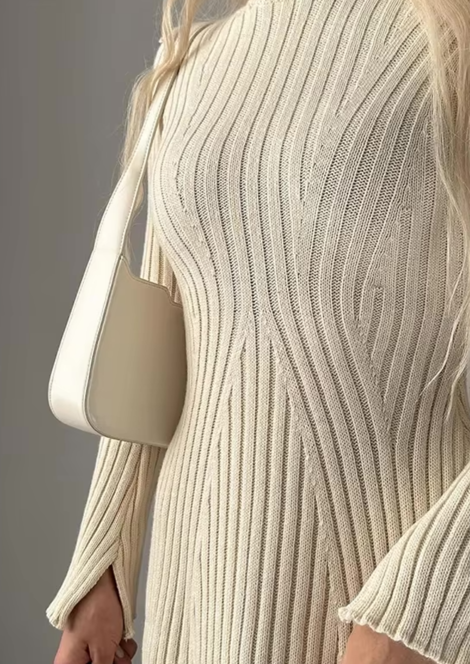 Close-up of the bodice of an ivory knit long sleeve ribbed mini dress, highlighting the vertical ribbing and a white shoulder bag.