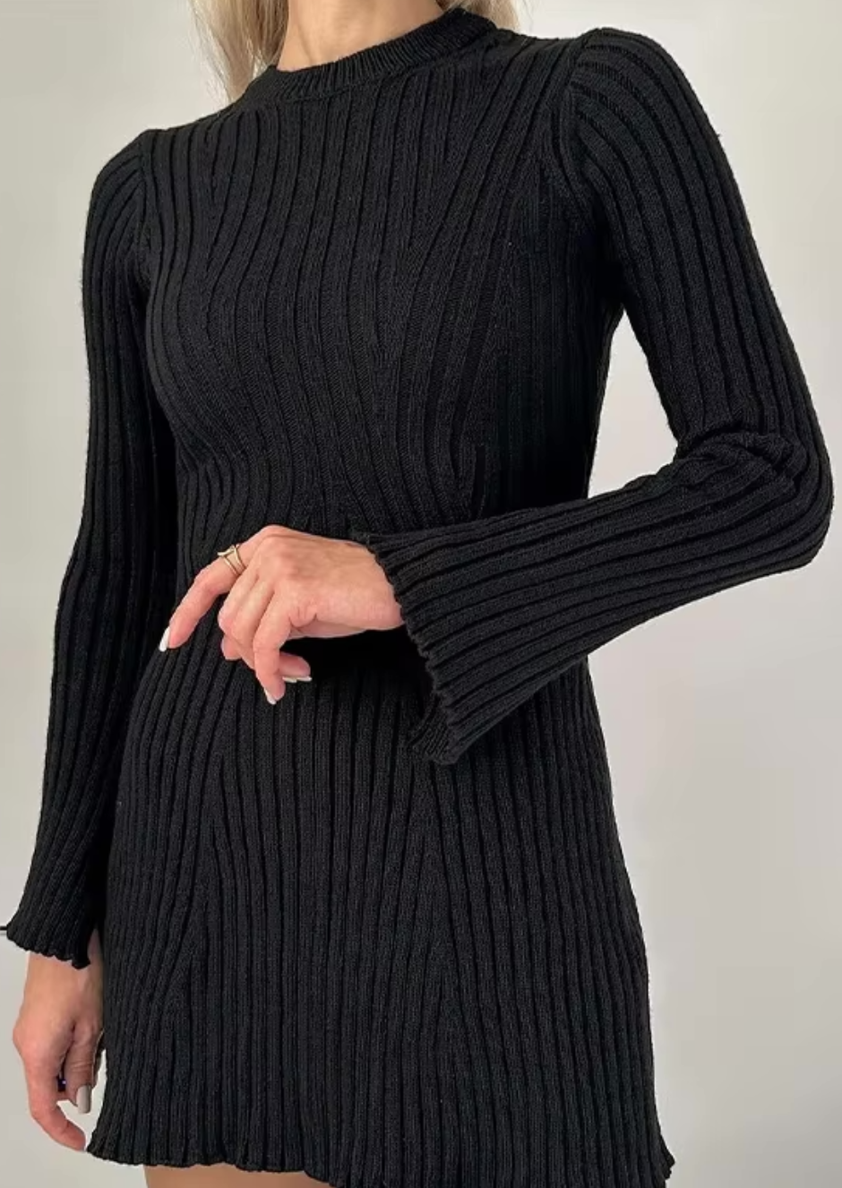Close-up of a woman's arm and torso in a black knit long sleeve ribbed mini dress, showing the flared cuff and ribbed texture.