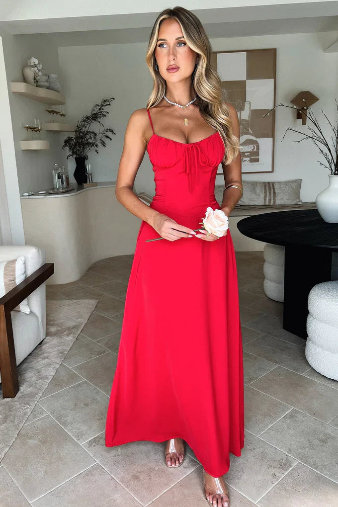 Front view of a woman in a vibrant red sleeveless maxi dress, featuring a lace-up bust detail and a full-length skirt, holding a rose.