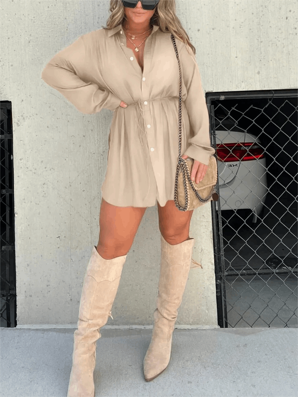 Beige long sleeve button front mini romper with drawstring waist, paired with knee-high suede boots and a chain strap purse.