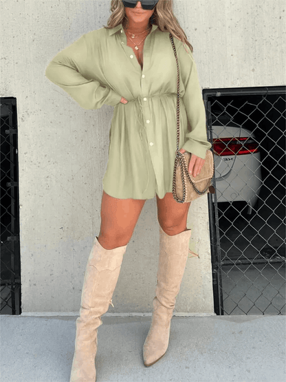 Sage green long sleeve button front mini romper featuring a collared design and adjustable waist, worn with tall boots.