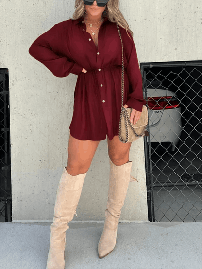 Burgundy long sleeve button front mini romper with cinched waist, paired with tall beige boots and a crossbody bag.
