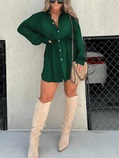 Emerald green long sleeve button front mini romper with cinched waist, styled with tall beige boots and a crossbody bag.