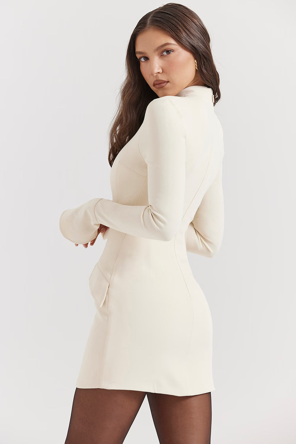 Side profile of a women's long sleeve high neck mini dress in cream with subtle pockets, showcasing the bodycon fit.
