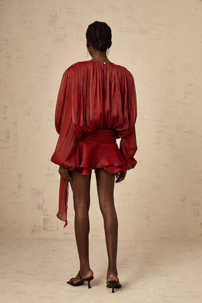 Back view of a women's long sleeve tie neck mini dress in a rich rust red color, featuring voluminous sleeves and a cinched waist with a long flowing belt.