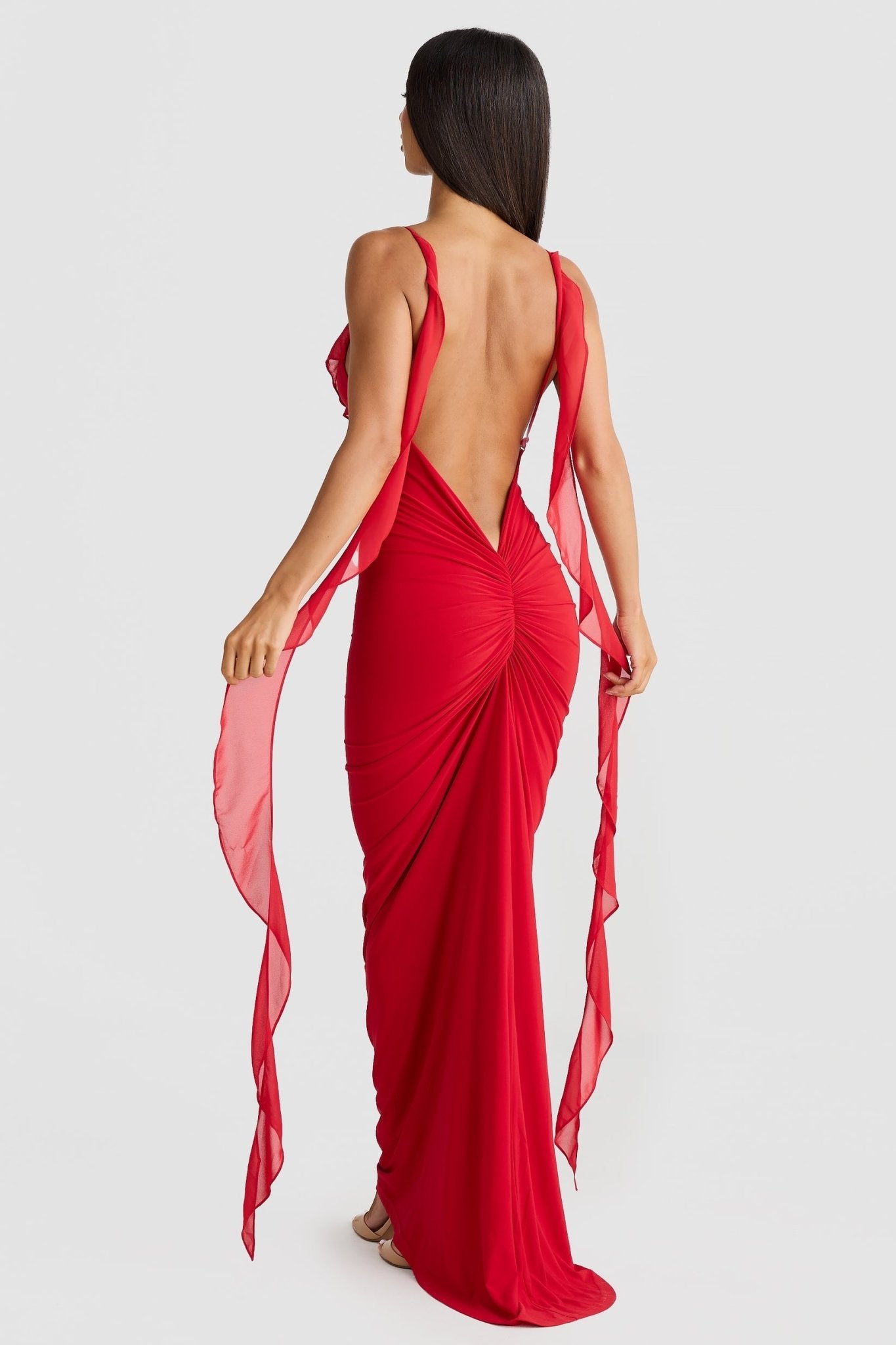 Back view of a red low back maxi dress with ruched detailing and flowing shoulder straps, elegant for wedding guests.