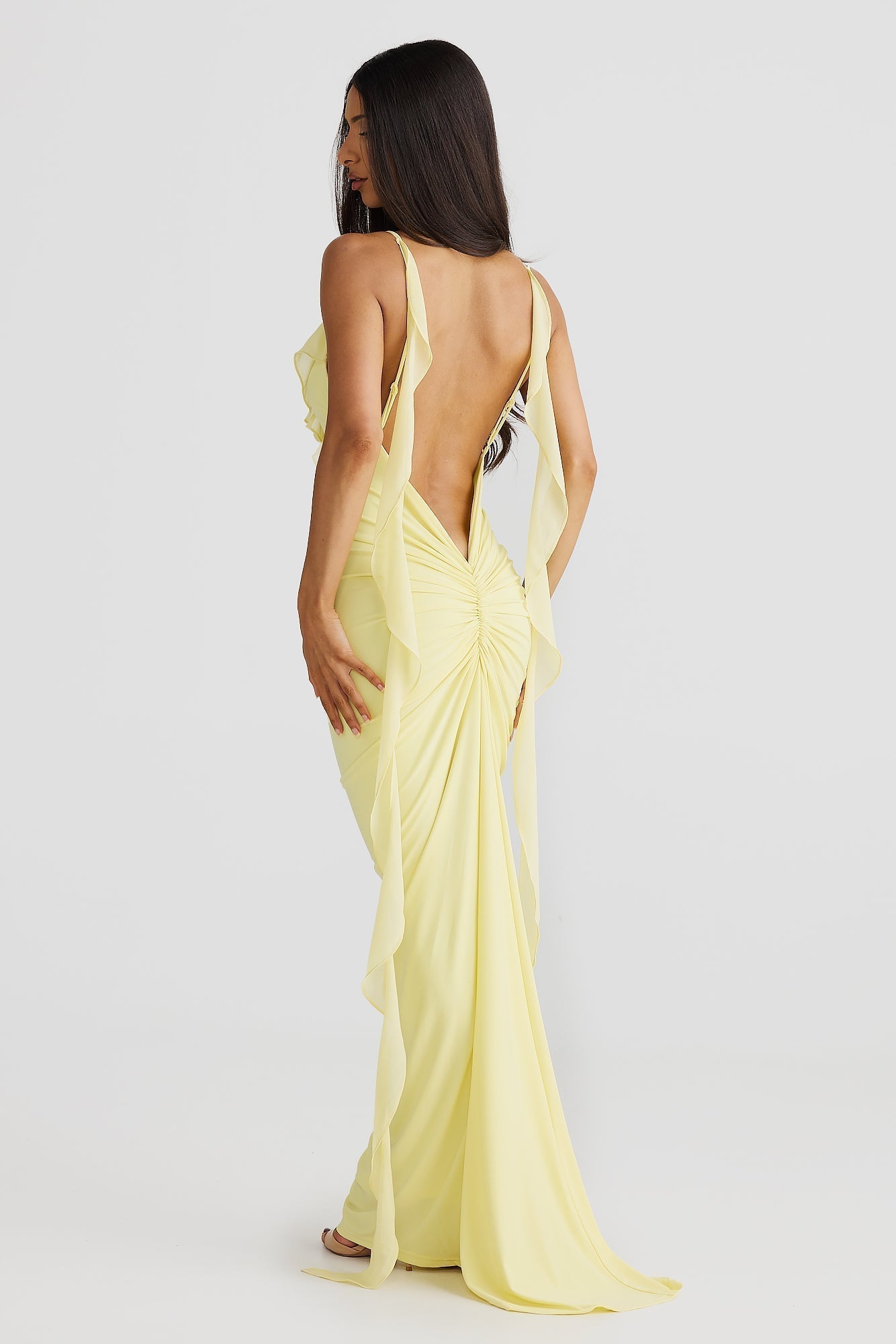 Back view of a yellow low back maxi dress featuring a ruched skirt and flowing straps, a beautiful vacation outfit.