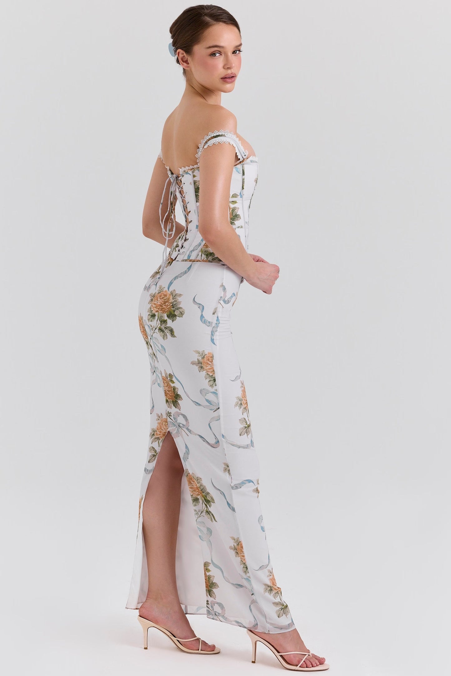 Side view of a women's off-shoulder corset floral maxi dress with a thigh-high slit, featuring orange roses and blue ribbons.