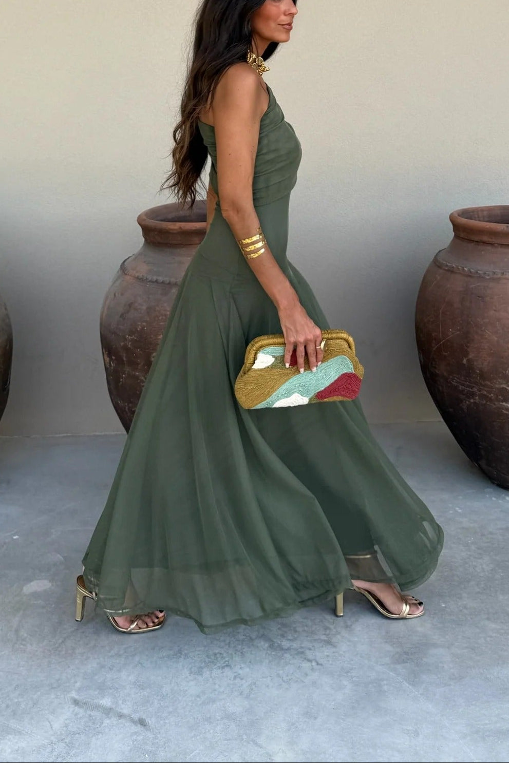 Side profile of a women's olive green off-shoulder draped mesh maxi dress, highlighting the flowing skirt and fitted bodice.