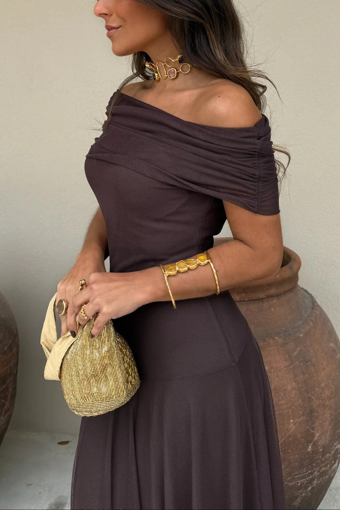 Side profile of a women's off-shoulder brown draped mesh maxi dress with ruched detailing on the sleeves and a subtle flowing skirt.