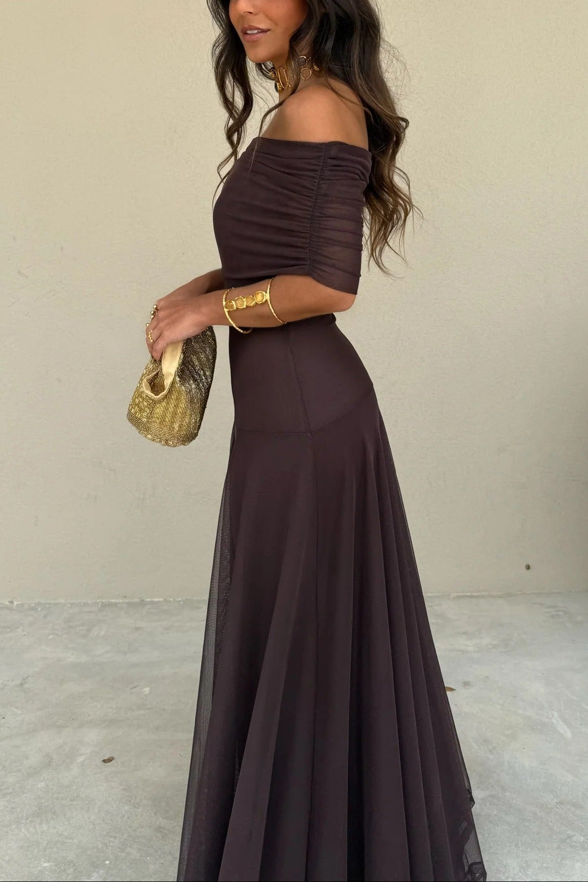Full side view of a brown off-shoulder women's draped mesh maxi dress, showcasing the sheer mesh overlay on the flowing skirt.