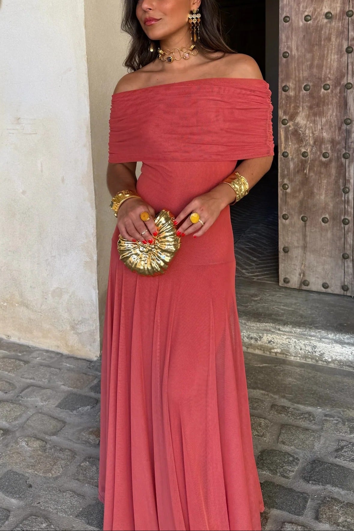 Front view of a women's off-shoulder draped mesh maxi dress in a vibrant coral pink, with a ruched bodice and flowing skirt.