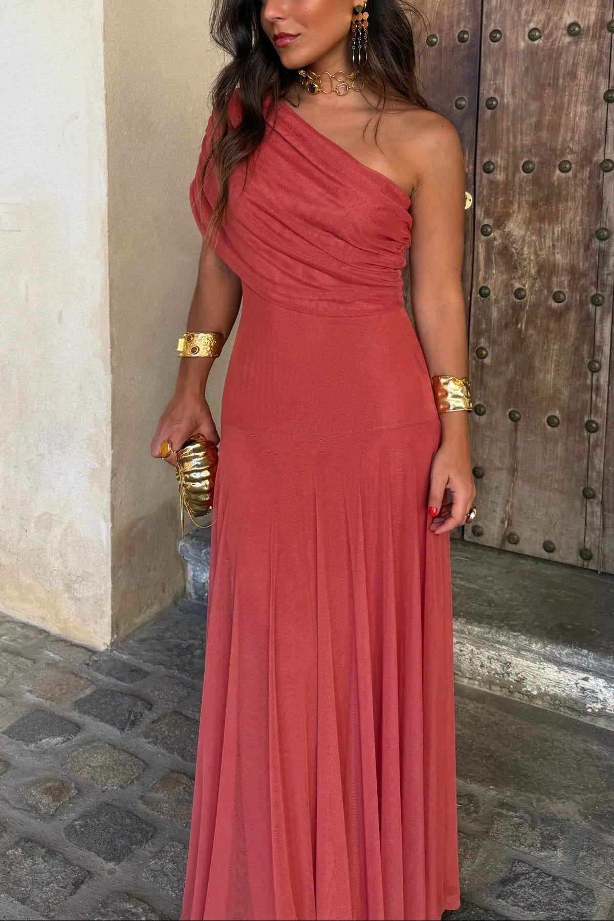 Women's coral pink off-shoulder draped mesh maxi dress with a one-shoulder design, showcasing the elegant drape and flowing silhouette.