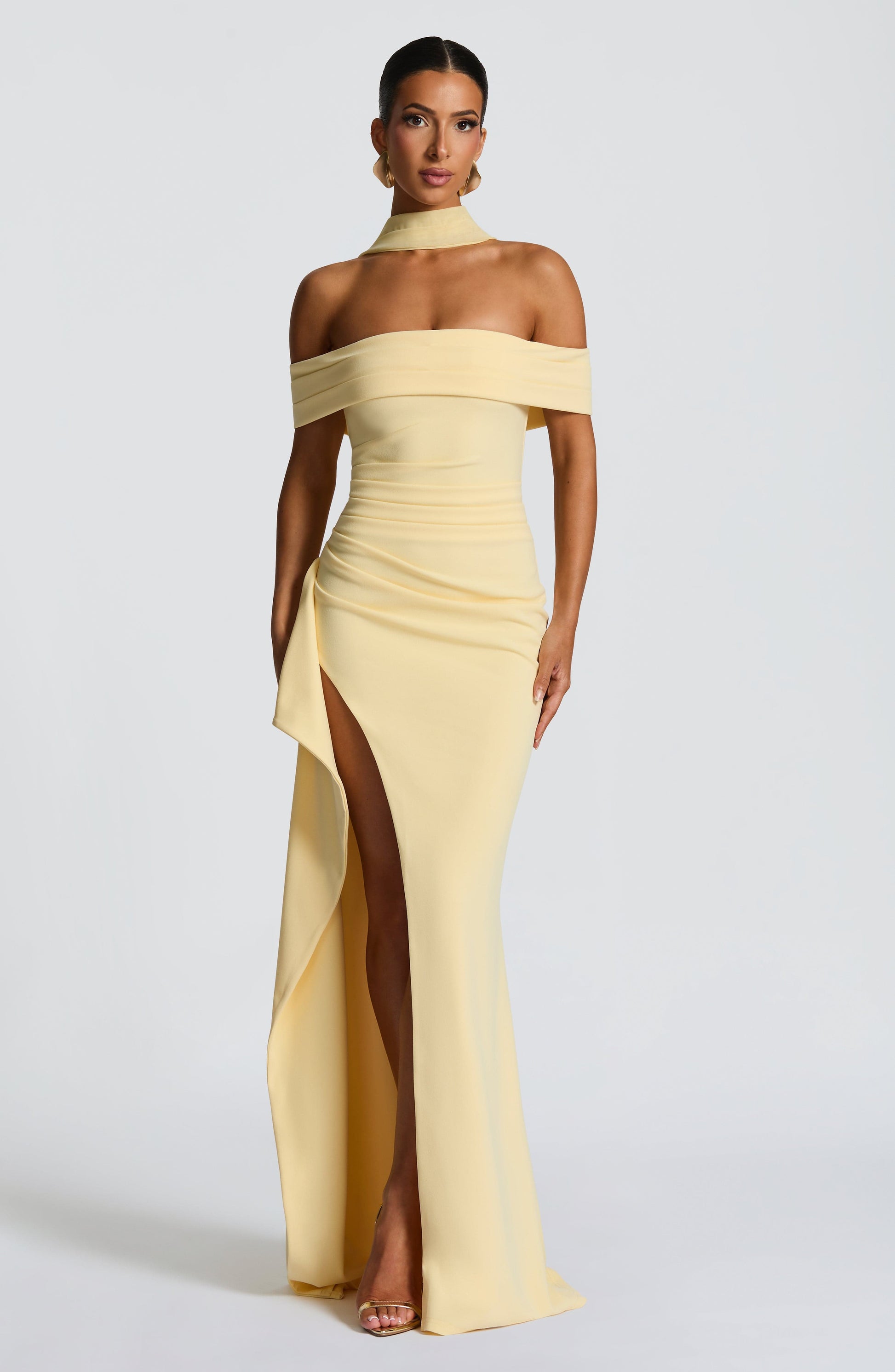 Full length view of a light yellow off-shoulder pleated maxi dress with a high slit and draped fabric accent.