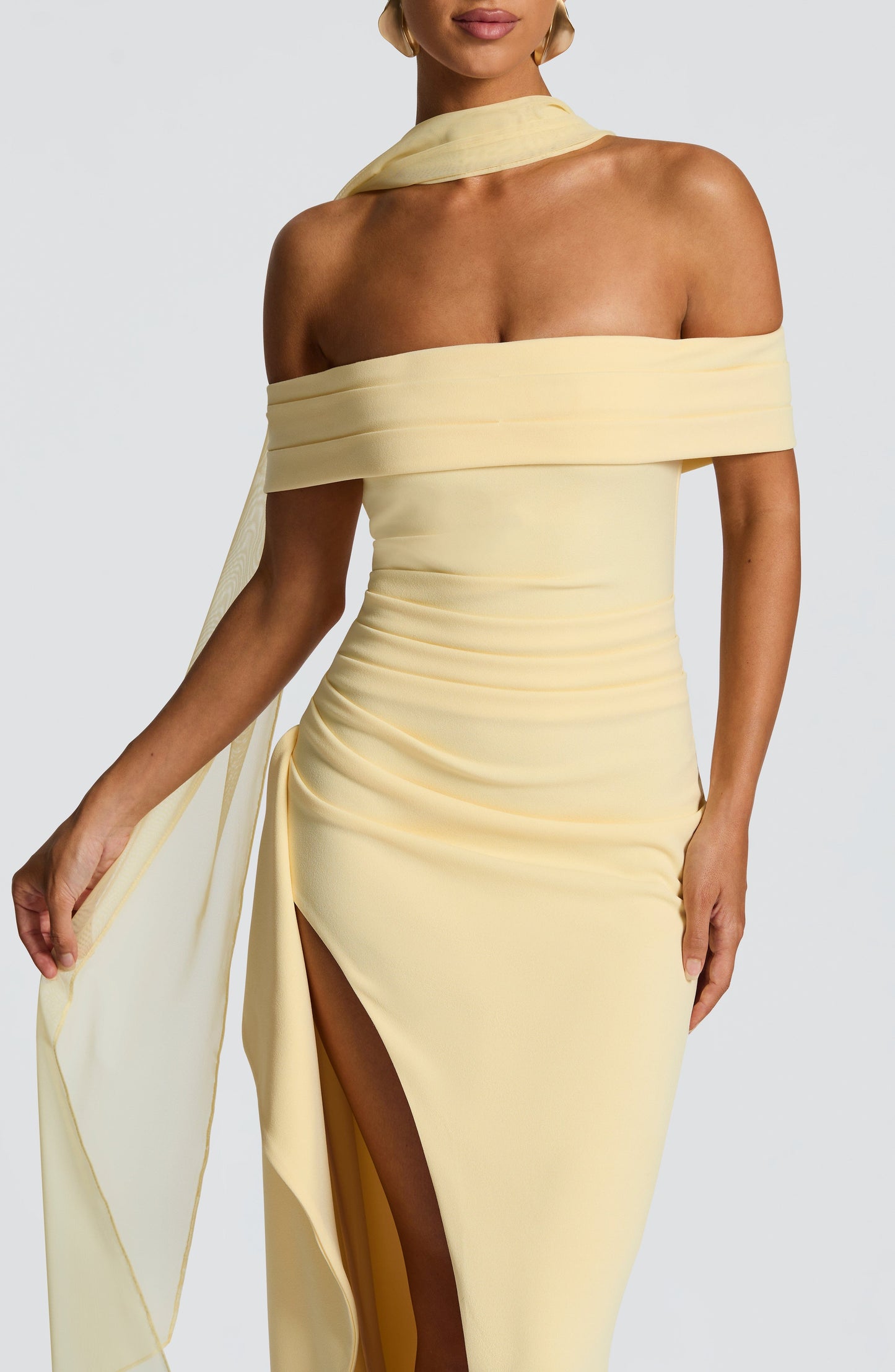Close-up of the light yellow off-shoulder pleated maxi dress, showing the draped fabric and high slit detail.