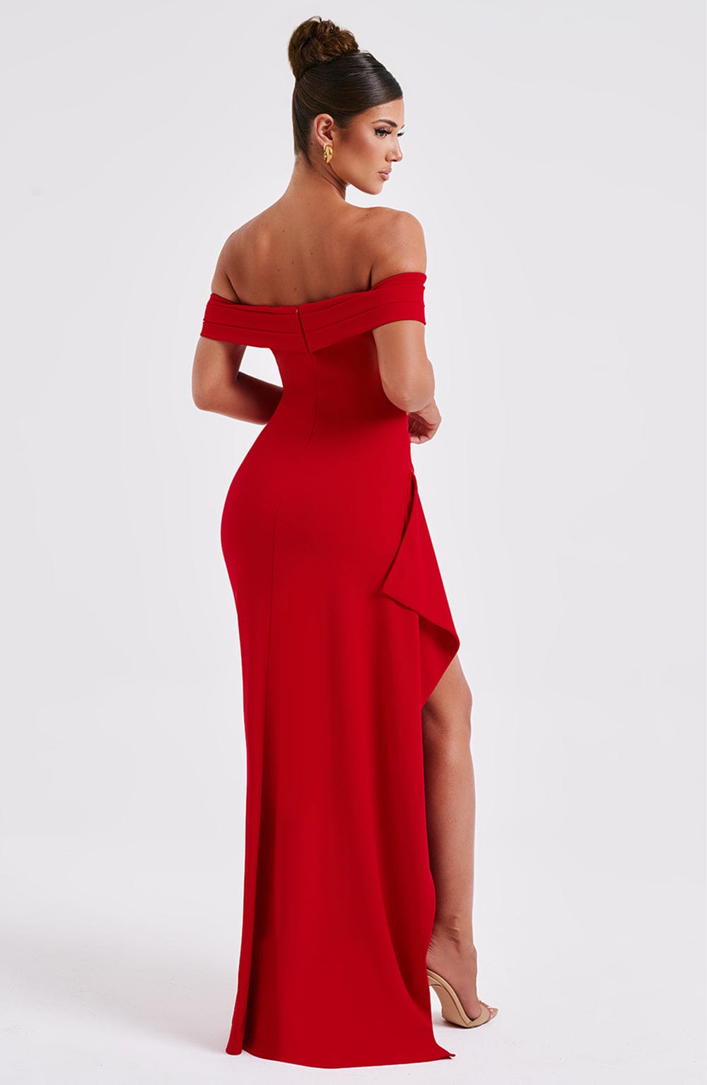 Back three-quarter view of the red off-shoulder pleated maxi dress, showing the leg through the high slit.