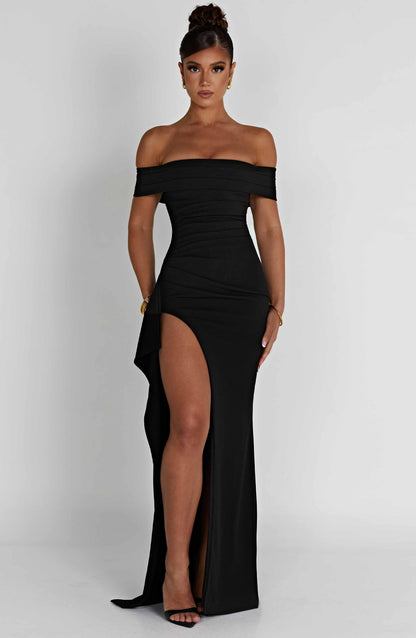 Full length view of a black off-shoulder pleated maxi dress with a high slit and fitted waist.